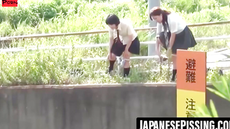 Two uniformed schoolgirls relieve themselves in the grass